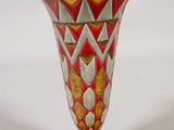 un vase rouge et doré posé sur une surface blanche