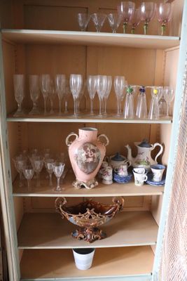 many glasses and vases on the shelves in this cabinet