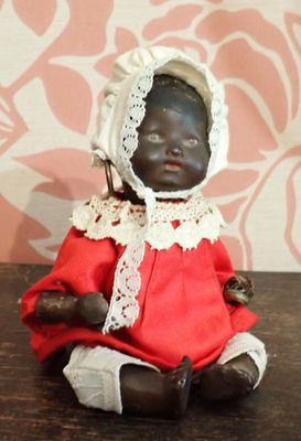 une poupée noire vêtue d'une robe rouge et d'un bonnet, assise sur une table