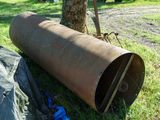 a large metal pipe laying in the grass next to a tree