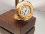 une horloge en or posée sur un socle en bois, elle-même posée sur une table en verre