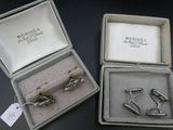 deux paires de boutons de manchette en argent dans un écrin posé sur un fond noir