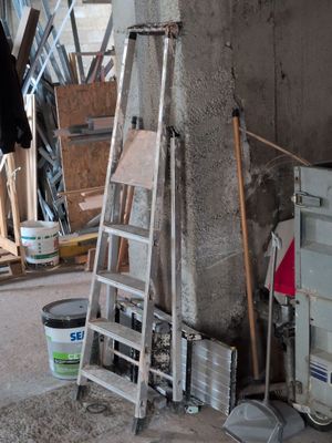 une échelle appuyée contre un mur, à côté d'un seau de peinture