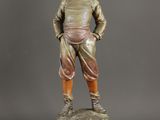 une statue en bronze représentant un garçon debout sur un socle en bois