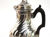 a silver coffee pot with a handle on a white surface