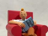 a figurine of a man sitting in a red chair reading a book