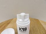 a bottle of k18 on a wooden table next to a cup
