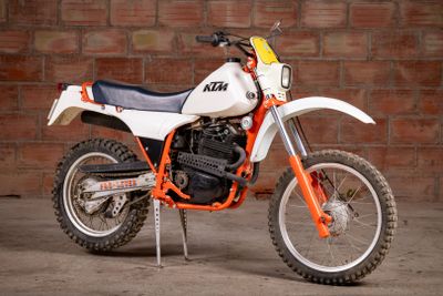 a white and orange dirt bike parked in front of a brick wall