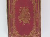 an old book with a red cover and gold trim on a white surface