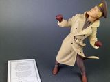 toy figurine of a man in a trench coat and hat holding an apple next to a piece of paper