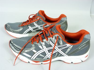 Des chaussures de course Asics sur un fond blanc, avec des lacets orange