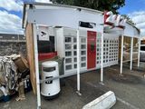 un bâtiment blanc avec une porte rouge, à côté d'un tas de vieilleries