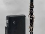 une clarinette noire et argentée à côté d'un étui noir sur fond blanc
