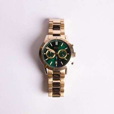 une montre en or avec un cadran vert posée sur une surface blanche