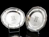 deux assiettes en argent ornées de monogrammes, posées sur un fond noir