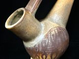 un vase marron muni d'une anse incurvée sur fond noir