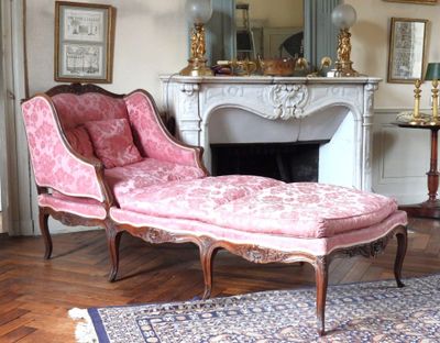 une chaise longue rose dans un salon avec une cheminée