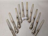 eight silverplated knives are arranged in a circle on a white surface