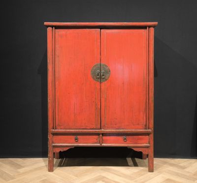 une vieille armoire rouge posée sur un parquet, près d'un mur noir