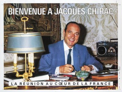 a man in a blue suit sitting at a desk in front of a lamp