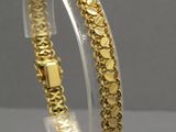 un gros plan d'un bracelet en or posé sur un socle transparent