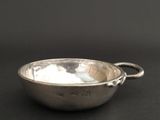 a silver bowl with a handle on a black surface
