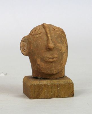 Tête en terre cuite rosée figurant un visage serein, au long…