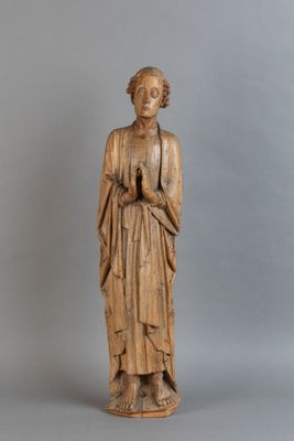 une vieille statue en bois représentant une femme, les mains dans les poches