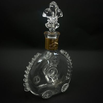 une bouteille en verre transparent avec un bouchon doré, posée sur une surface noire