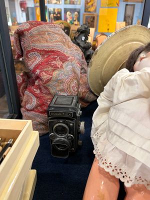 une poupée avec un chapeau et un appareil photo, à côté d'une vitrine