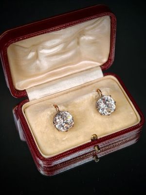 deux paires de boucles d'oreilles en diamant dans un écrin rouge posé sur un fond noir