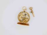 a close up of a pocket watch with a key on a white surface