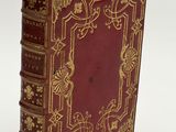 an old red book with gold trim sitting on top of a white surface