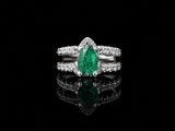 un gros plan d'une bague sertie d'une émeraude verte et de diamants, posée sur une surface noire