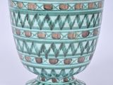 un vase vert orné d'un motif sur un fond blanc