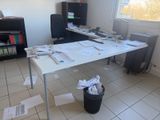 un bureau recouvert de papiers et une poubelle au milieu de la pièce