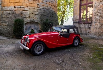 une voiture rouge et noire garée devant un bâtiment en pierre