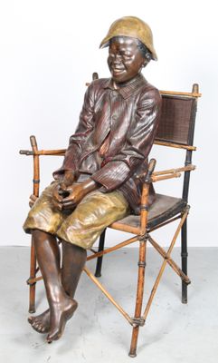 statue en bronze représentant un homme assis sur une chaise, coiffé d'un chapeau