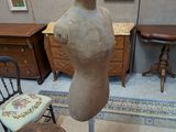 un mannequin posé sur un socle dans une pièce où sont accrochés des tableaux aux murs