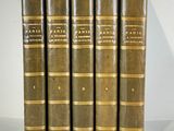 five antique books are lined up in a row on a white surface