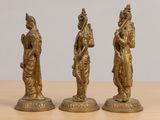three brass figurines of a woman and a man on a wooden table