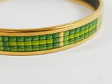 a close up of a green and gold bracelet on a white surface