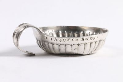 une vieille coupe en argent munie d'une anse, posée sur une surface blanche