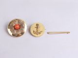 two gold and coral colored buttons and a pin on a white surface