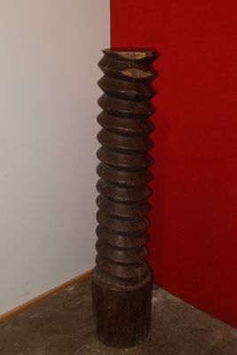 a tall wooden vase sitting in a corner of a room