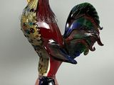 une statue colorée représentant un coq, posée sur un socle, sur fond blanc