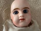 a small doll with blue eyes sitting on a carpet
