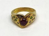 une image représentant une bague en or sertie d'une grenat en forme de cœur, entourée de pierres vertes et violettes