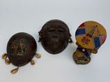 trois masques africains sont posés les uns à côté des autres sur une surface blanche