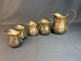 five antique silverplated jugs and a pitcher on a grey background